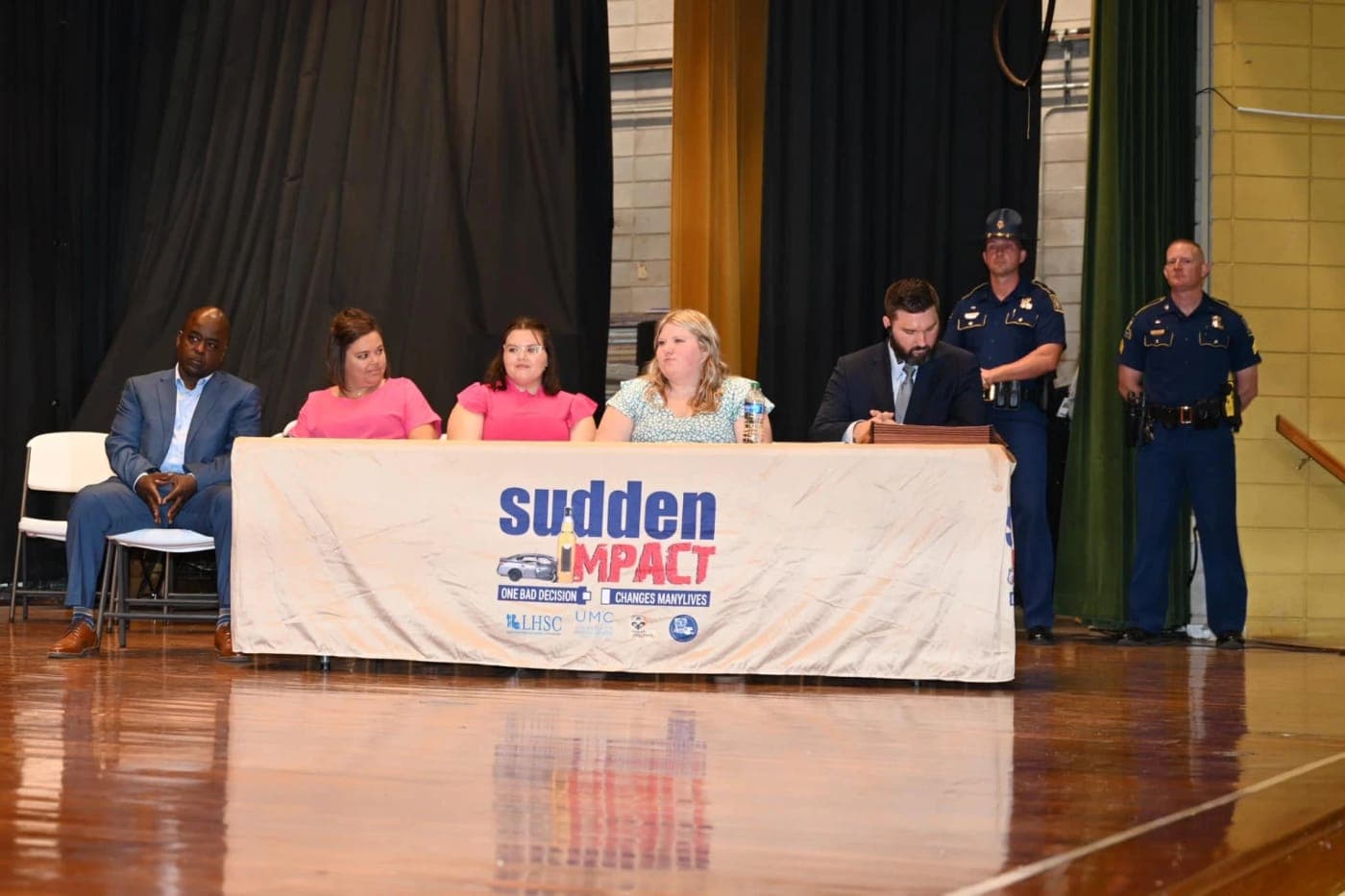 Stephen Spurgeon seated at the Sudden Impact table on stage with Louisiana State Troopers standing behind